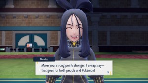 a dark haired woman in a jumpsuit standing in a large gymnasium. dialogue at the bottom reads "Make your strong points stronger, I always say - that goes for both people and Pokemon!"
